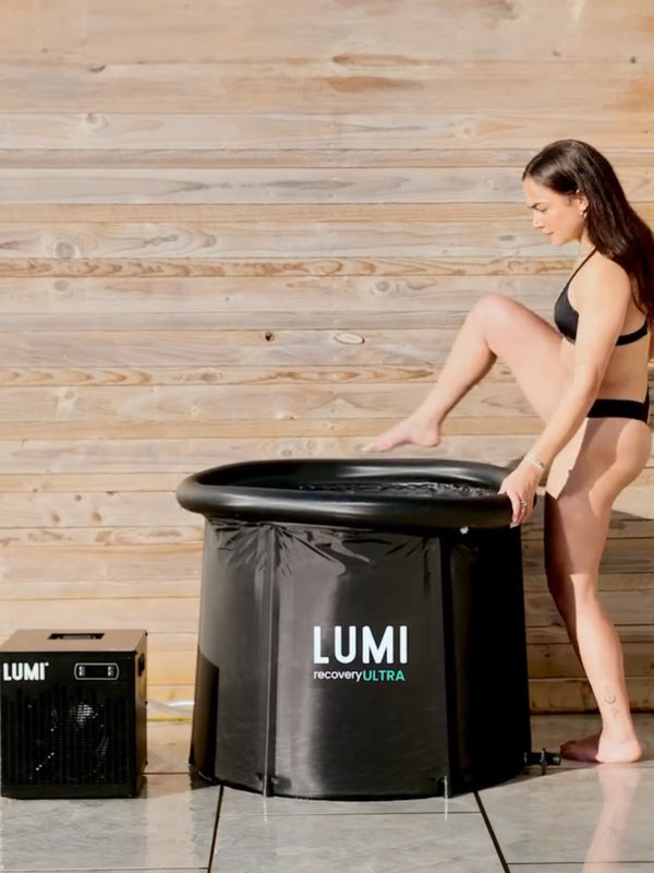 A woman wearing a black swimsuit stepping in a LUMI MAX Ultra ice bath