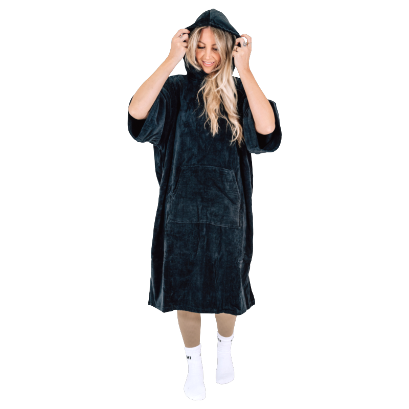 Woman wearing black LUMI Towel Poncho Changing Robe from Cold Club Starter Set adjusting hood and smiling